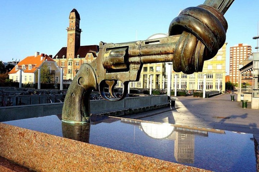 A large metallic sculpture of a revolver on a reflective surface with a historic building in the background. 5