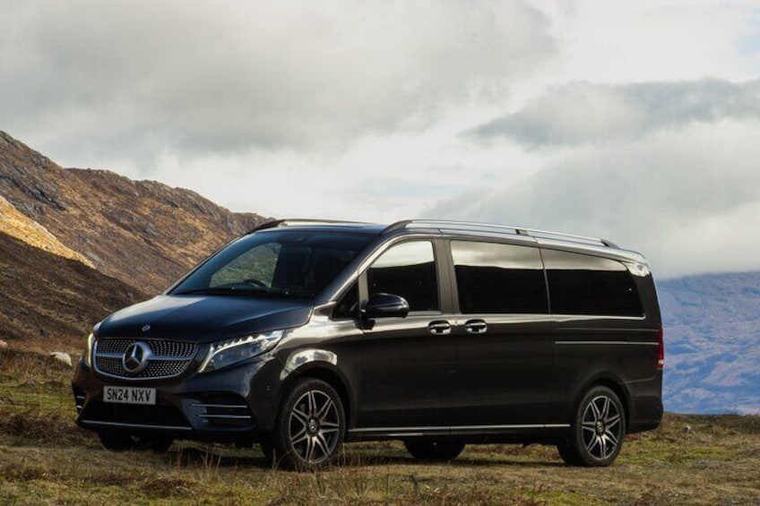 A dark-colored SUV parked on a grassy field with mountains in the background. 2