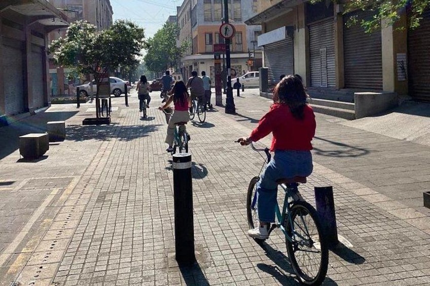 A person riding a bicycle on a paved street with buildings and trees in the background. 4