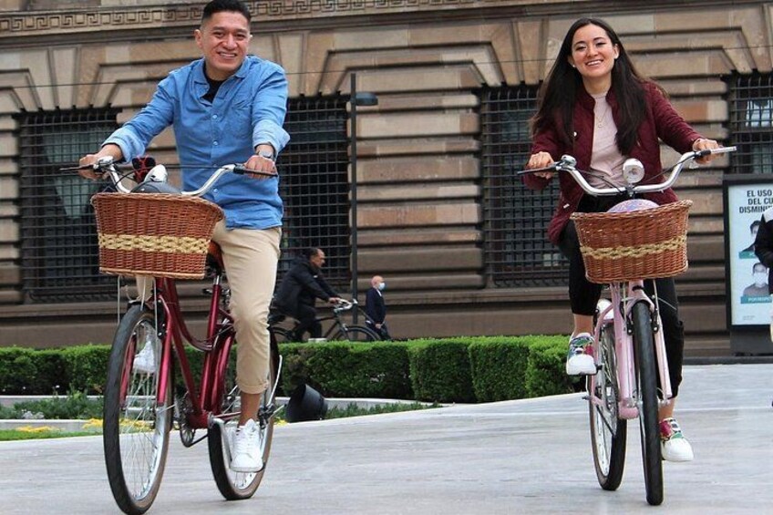 Two people riding bicycles with baskets on a paved path. 3
