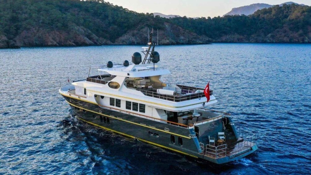 A large yacht on calm waters with a forested shoreline in the background. 3