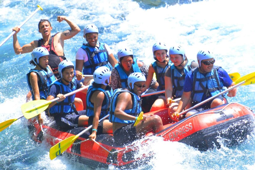 A group of people in a red inflatable raft on a river, wearing helmets and life vests. 2
