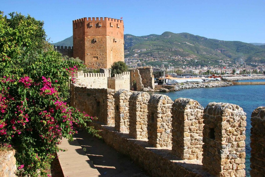 A historic stone wall with a tower, a coastal town, and mountains in the background. 5