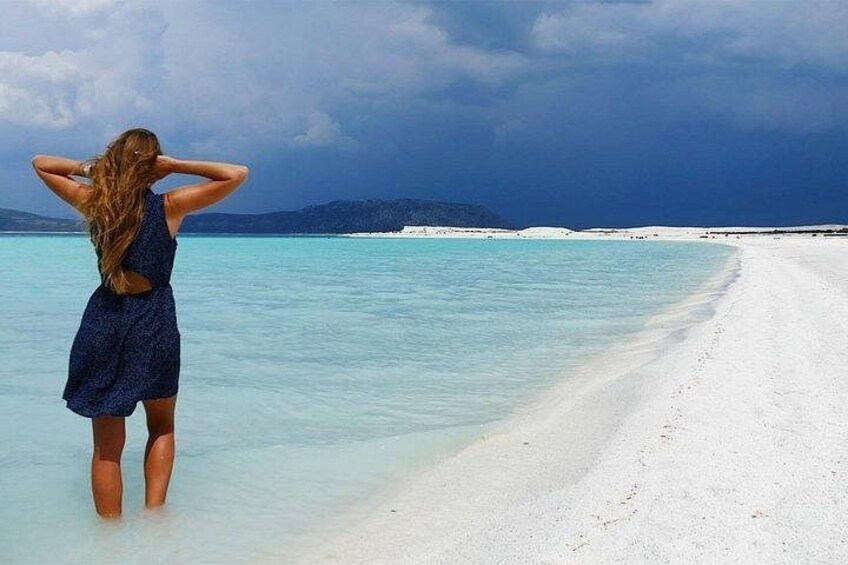 En kvinde står på en hvid sandstrand og ser ud over et turkisblåt hav under en klar himmel. 4