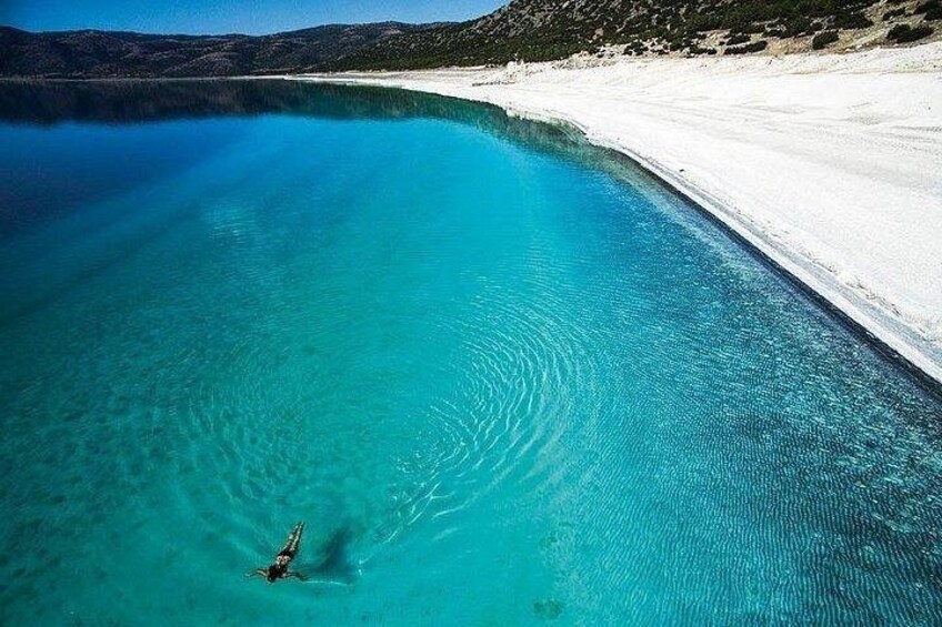 En klar turkis pool med en person, omgivet af hvid sand og bakker. 2