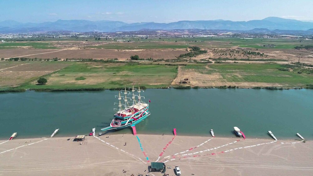A large cruise ship docked at a port with a clear view of the surrounding landscape, including fields and distant mountains. 2