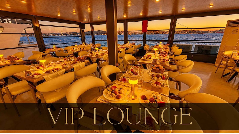 A VIP lounge with tables set for dining, overlooking a body of water with a cityscape in the background. 5