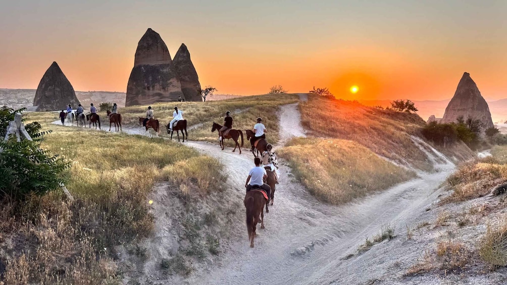 A group of people horseback riding on a dirt path with unique rock formations in the background. 1