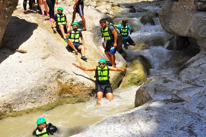 People in life vests and helmets navigating a rocky stream. 4