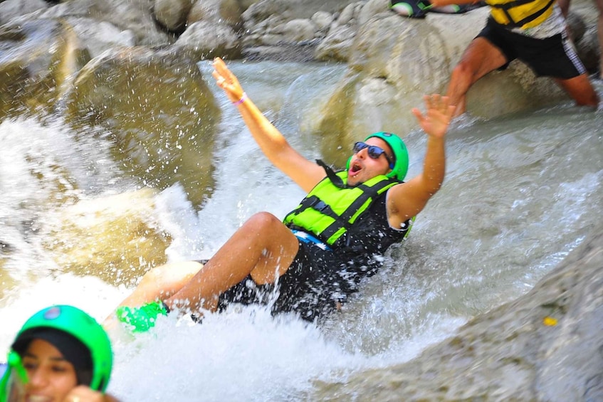 A person in a green helmet and life jacket sliding down a water slide. 1