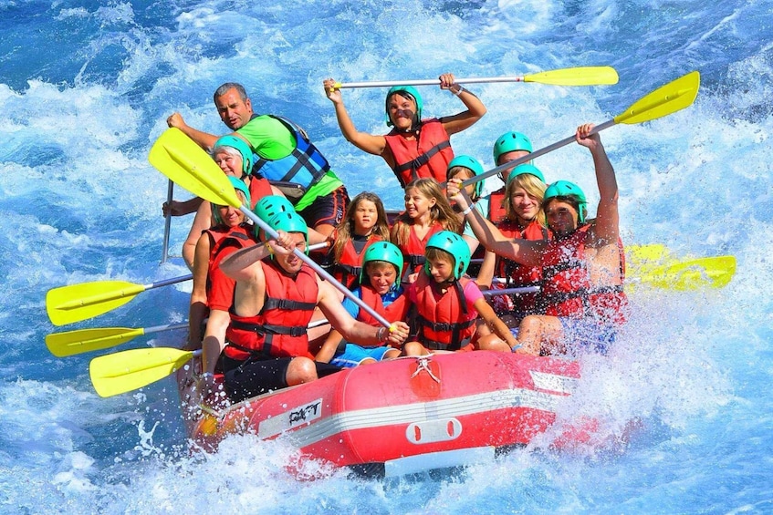 A group of people in a red raft with yellow paddles, wearing helmets and life jackets, navigating through rough water. 5