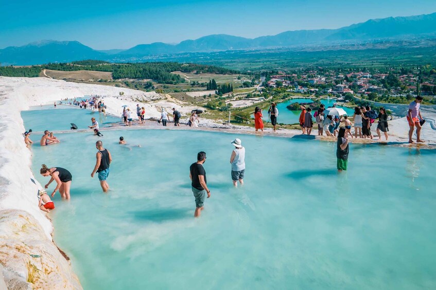 People enjoying a hot spring pool with a scenic view of mountains and a town in the background. 1