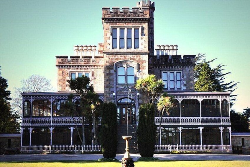 A large, historic stone building with a central tower, symmetrical windows, and a decorative fence. 1