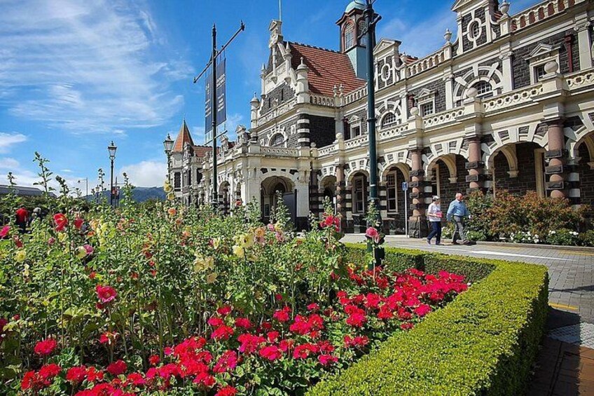 A historic building with ornate architecture, a well-maintained garden with red flowers, and a clear blue sky. 2