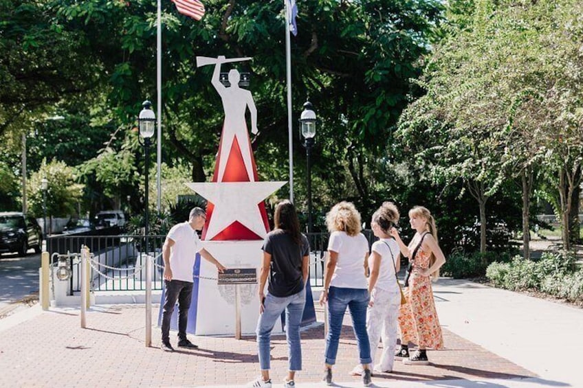 Un grupo de personas junto a una estatua con una estrella roja y una figura sosteniendo una antorcha. 2