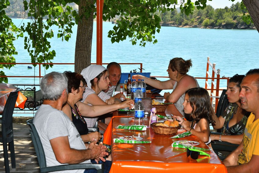 Eine Gruppe von Menschen speist an einem Tisch im Freien am See. 2