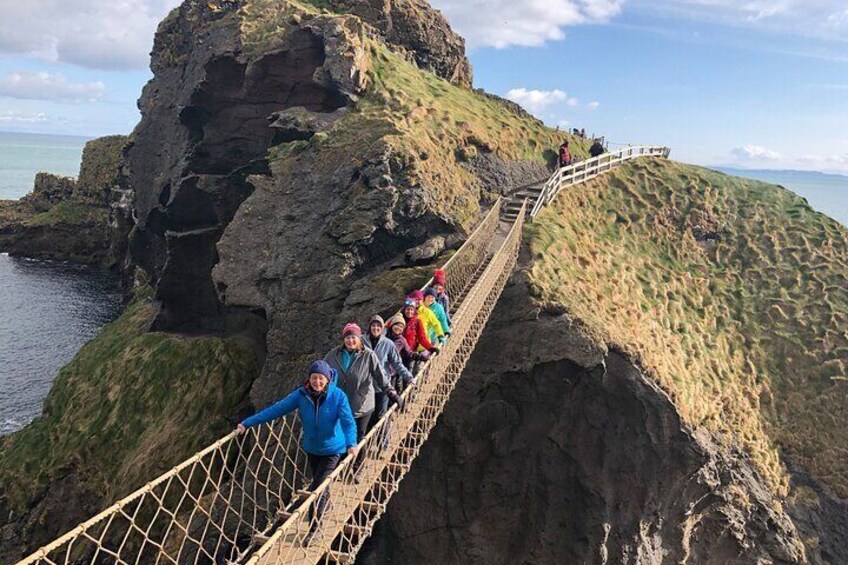 A group of people on a rope bridge over a rocky cliff by the sea. 1