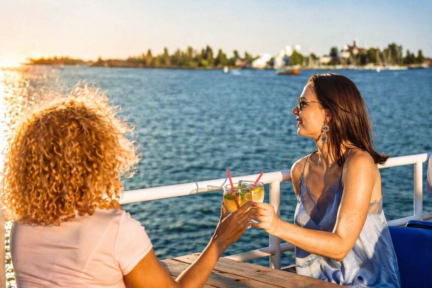 Två personer sitter vid ett bord intill ett vattendrag och håller i varsin drink. 2