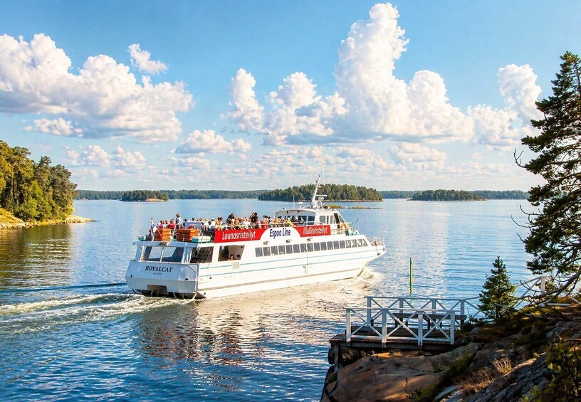 En färja med namnet ”ROYALCAT” som har logotyperna ”Lounasriistilyt” och ”Espoo Line”, färdas på en stilla sjö med en brygga och träd i förgrunden. 5