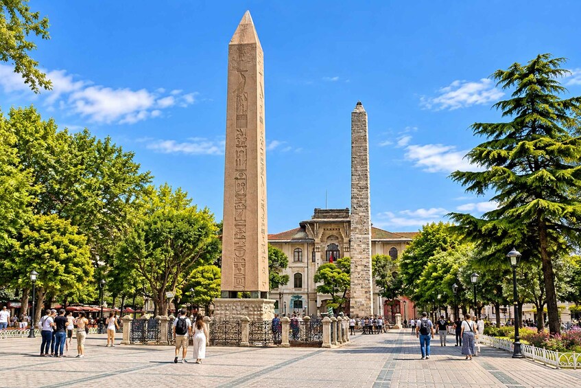 Two obelisks in a square with trees and a building in the background. 4