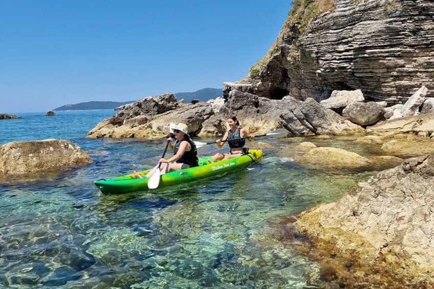 Two people kayaking on clear water with rocky terrain and cliffs in the background. 5