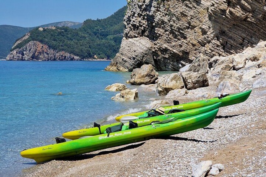 Two green kayaks on a rocky beach with clear blue water and a mountainous backdrop. 2