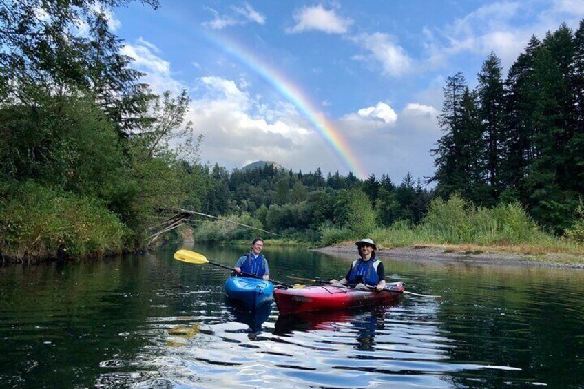 Two people kayaking on a river with a rainbow in the background. 2