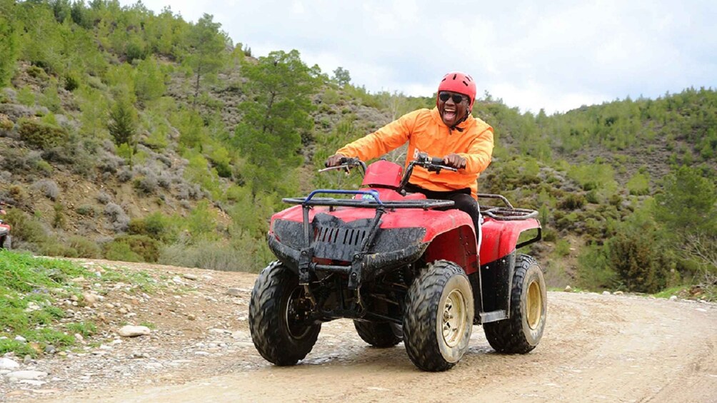 En person kører på en rød ATV på en grusvej omgivet af grønt. 2