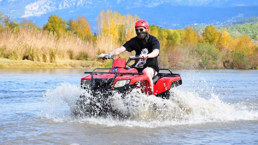 En person kører på en rød ATV i en flod. 1