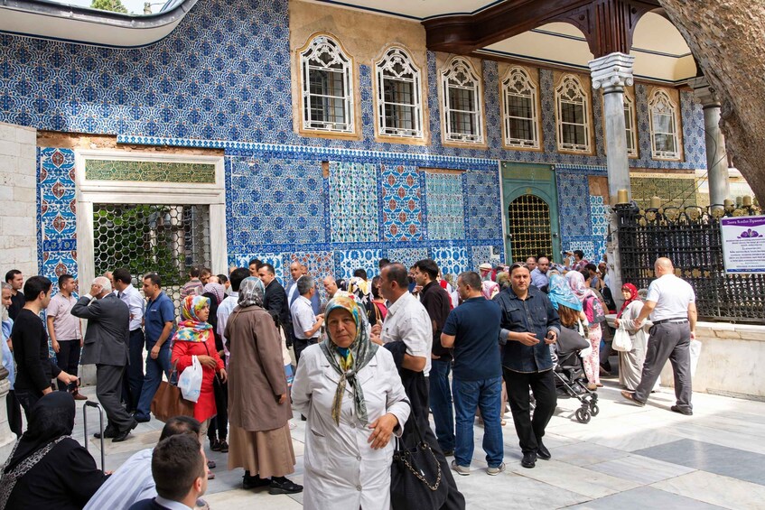 A crowd of people gathered outside a building with intricate blue and white tile patterns and arched windows. 5
