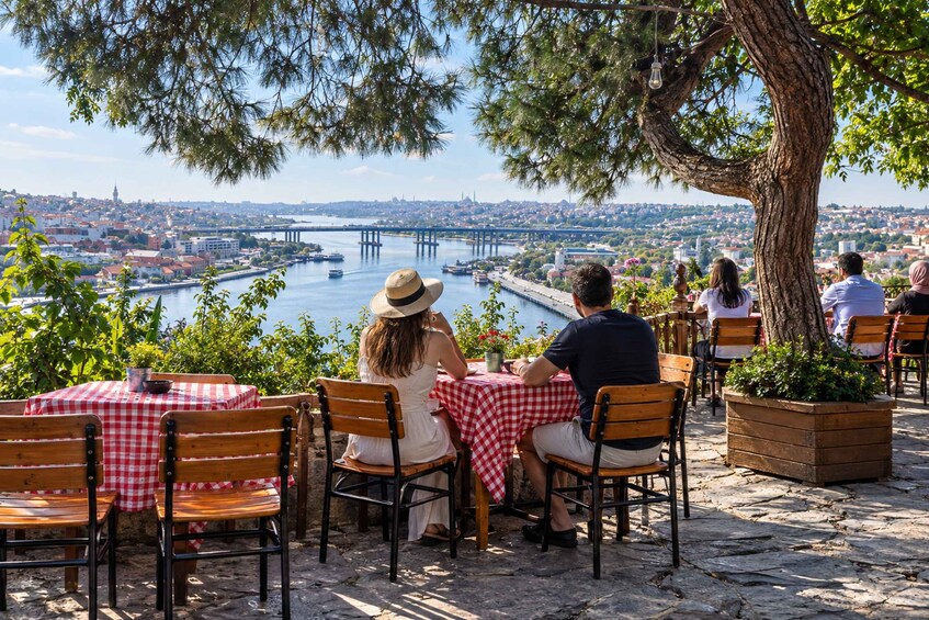 Una pareja cenando en un café al aire libre con vistas panorámicas a un río y un puente. 5