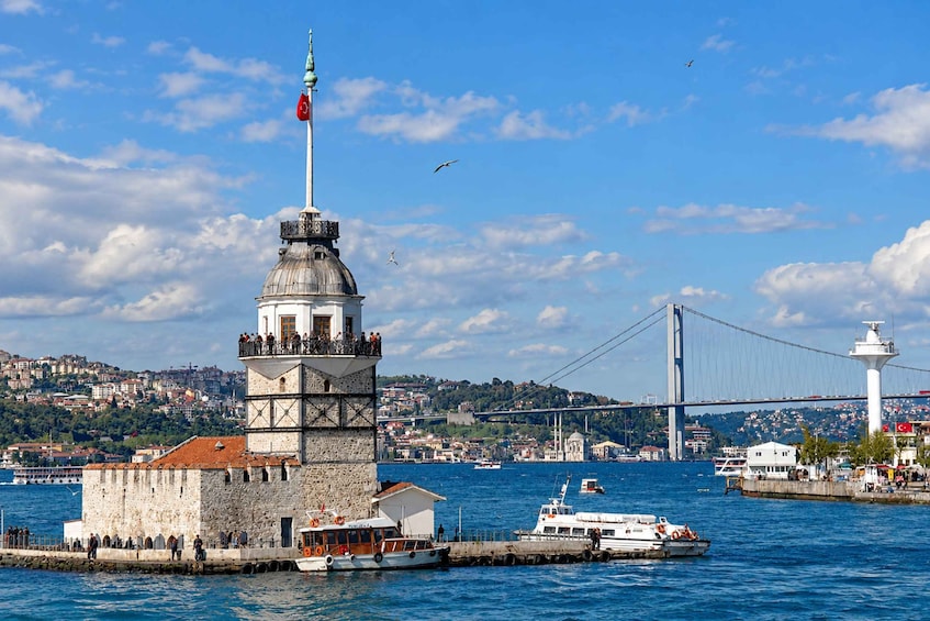 Una torre histórica con una bandera, un puente y un cuerpo de agua con barcos. 3