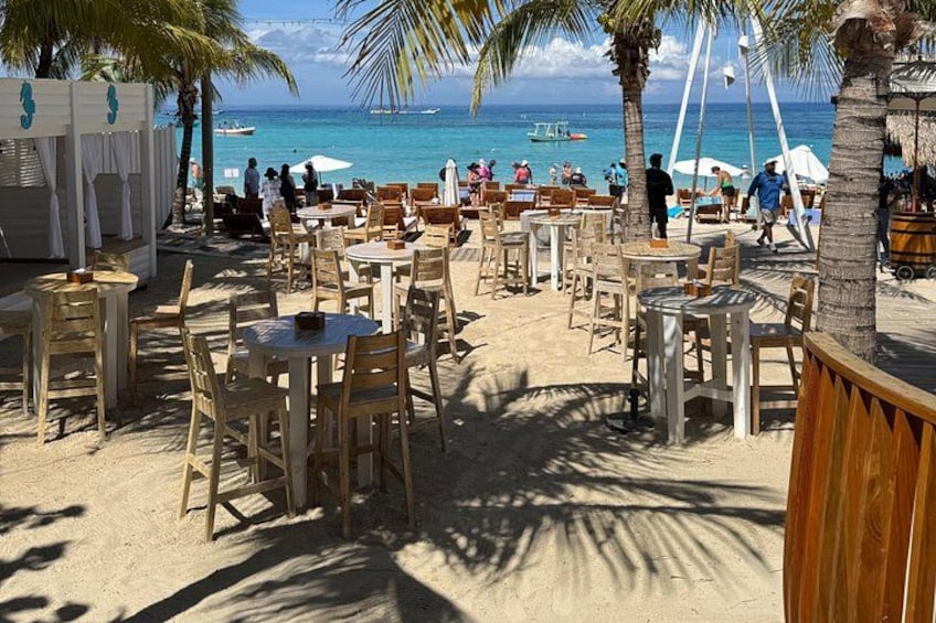 A beachside café with tables and chairs, palm trees, and the ocean in the background. 3