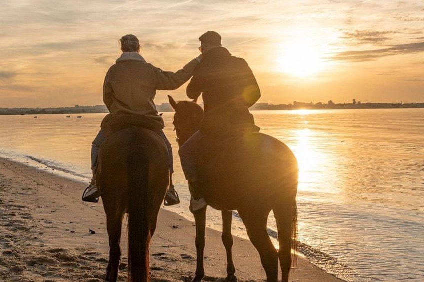 To personer rider på heste ved en strand i solnedgangen. 1