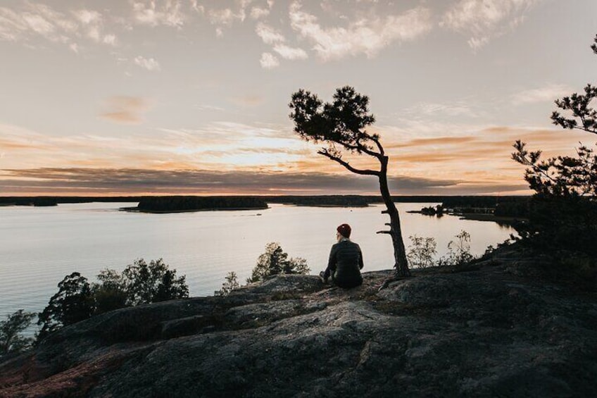 A person sitting on a rock by a calm lake during sunset. 1