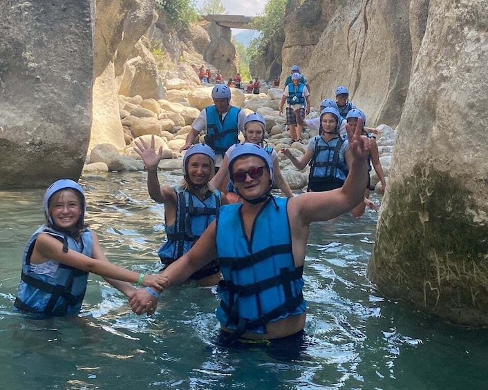 A group of people in blue life vests wading through a narrow river surrounded by rocky cliffs. 2
