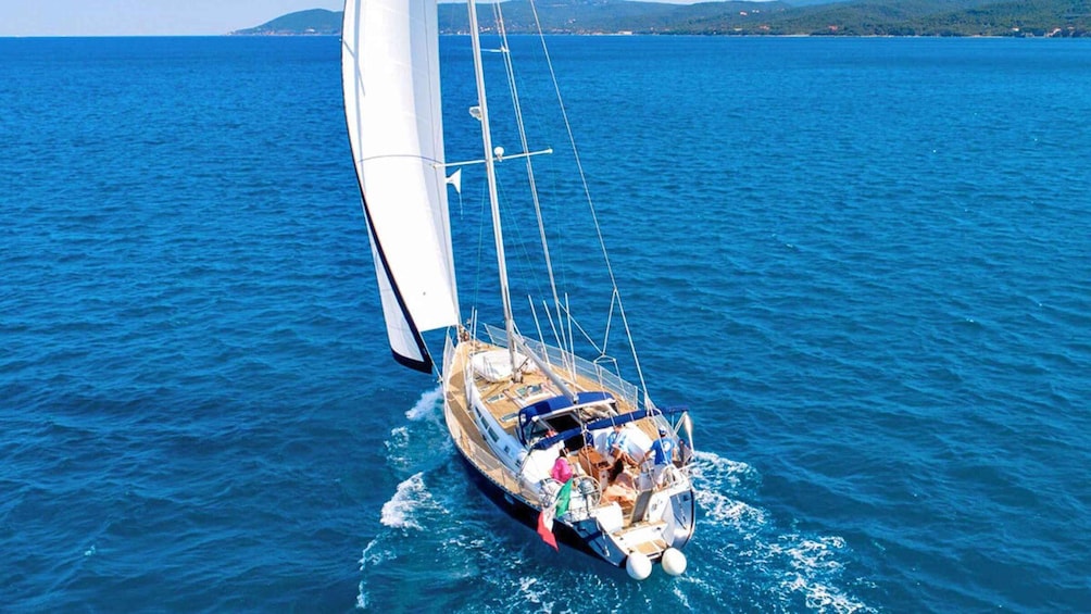 A sailboat on a blue sea with a mountainous coastline in the background. 1