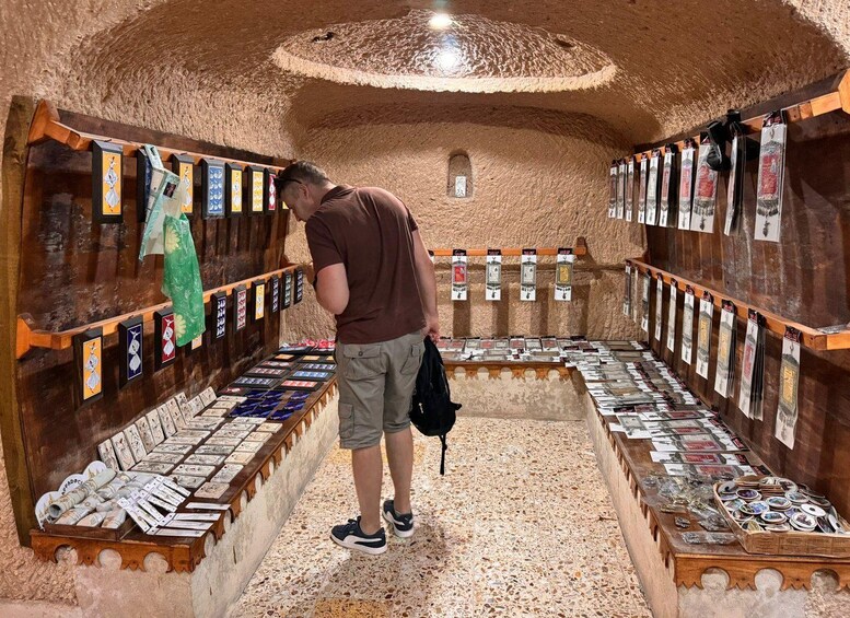 A man browsing through a collection of postcards and cards in a cave-like setting with wooden shelves. 3