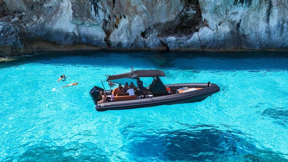 Ein Boot mit Personen auf ruhigem, blauem Wasser nahe einer felsigen Klippe. 3