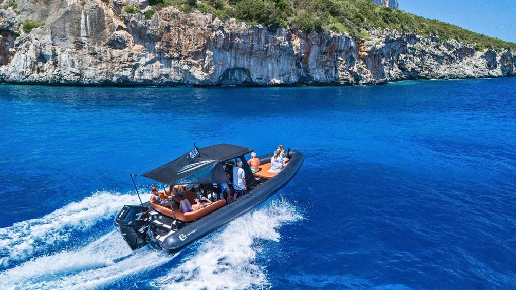 Ein Motorboot mit Passagieren auf blauem, klarem Meer, im Hintergrund steilen Felsen. 1