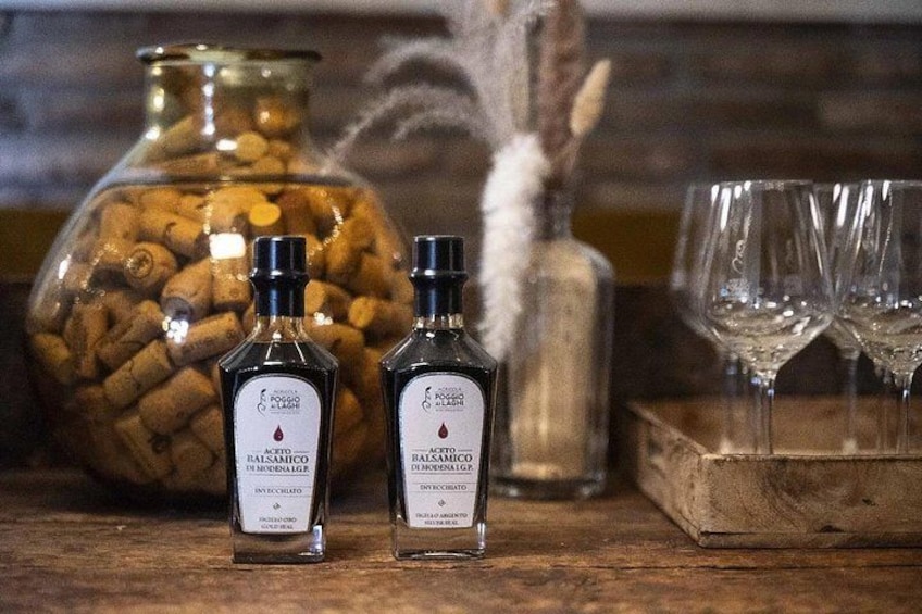 Två flaskor balsamvinäger, en glasburk med korkar och två tomma vinglas på en träyta. 3