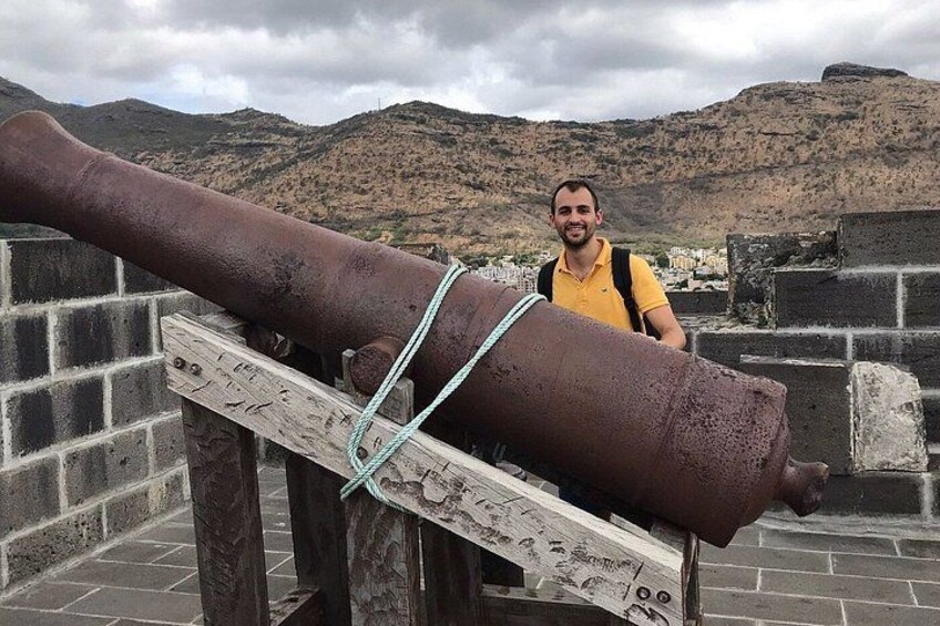 A large cannon on display, a person standing behind it, and a mountainous landscape in the background. 5