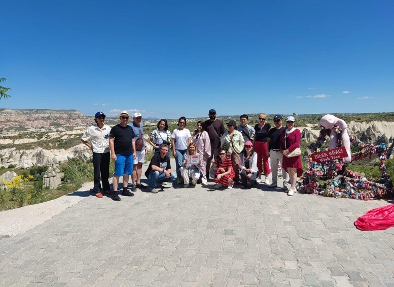 En gruppe mennesker står på en belagt plads med et bjergrigt landskab i baggrunden. 2