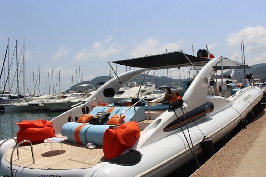 Una lancha inflable blanca amarrada en un puerto deportivo, con cojines anaranjados y un toldo. 1