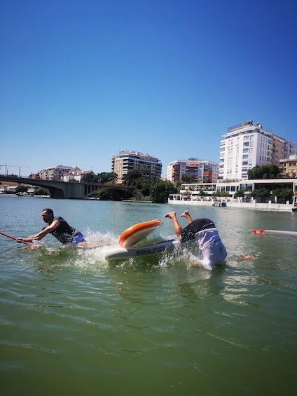 Due persone praticano wakeboard su un fiume, con edifici sullo sfondo. 3