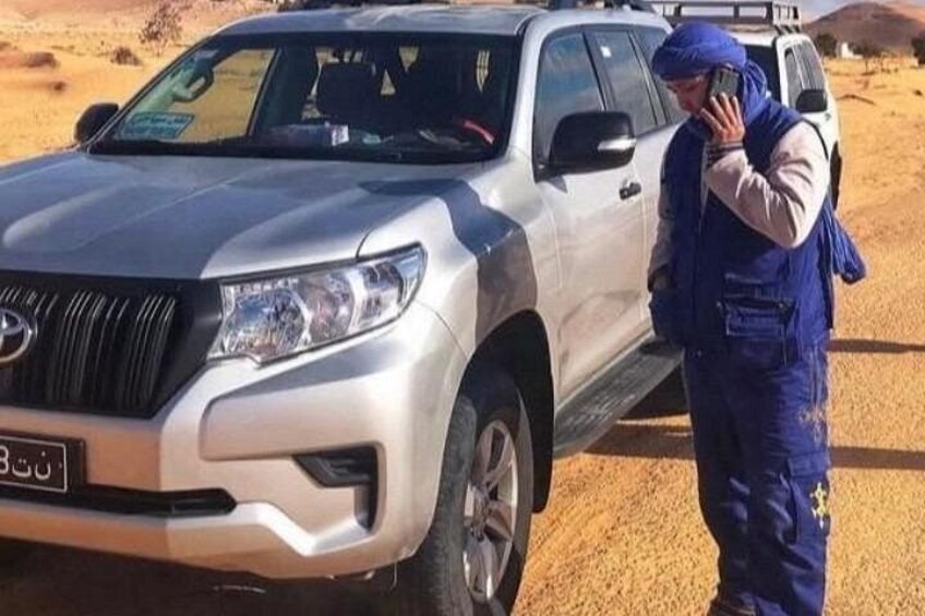 A silver SUV parked in a desert with a person in blue overalls standing beside it. 2