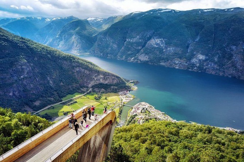 En träbro med människor som går över den, med utsikt över en fjord och berg. 2