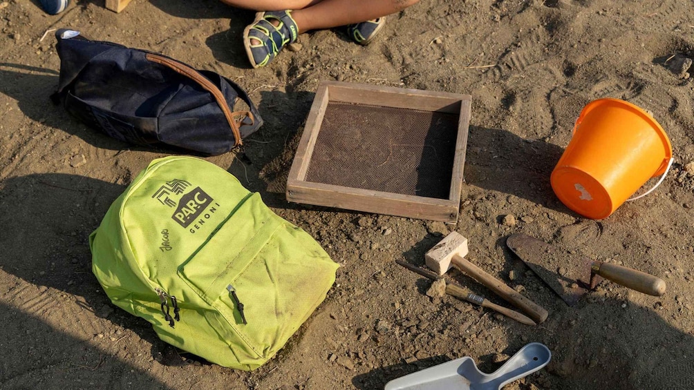 A beach with a green bag, a wooden frame, a shovel, a bucket, and a pair of sandals. 5