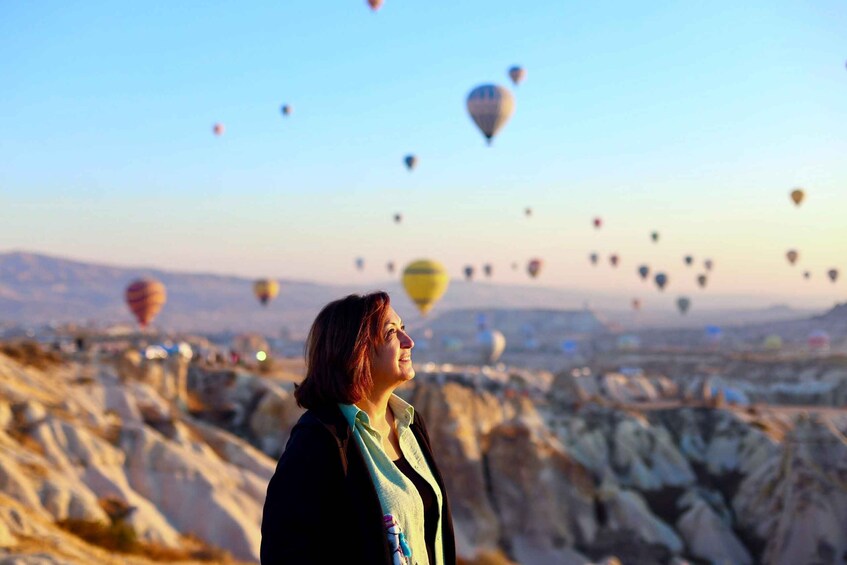 A person standing with a view of multiple hot air balloons in the sky. 4