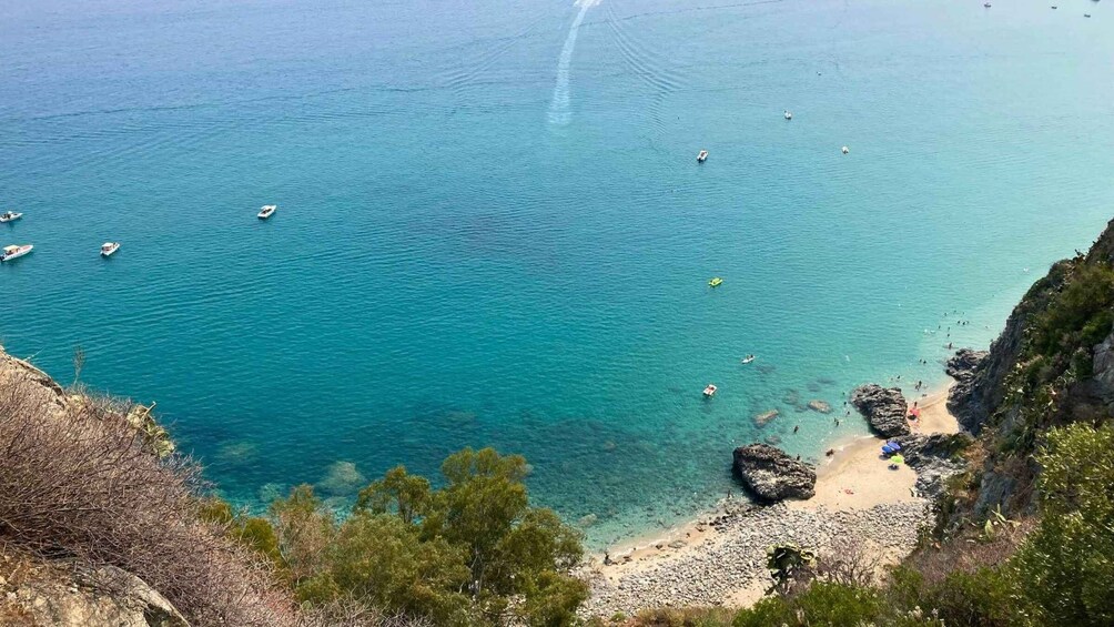 A coastal landscape with clear turquoise waters, boats, and a rocky beach. 2